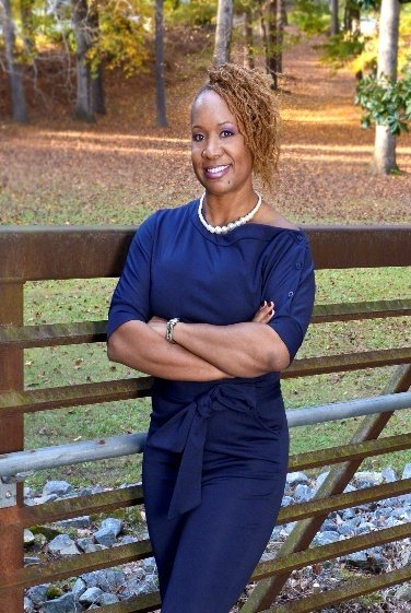 LaTasha Bond Williams with arms crossed, smiling on a footbridge in autumn